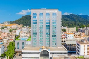 A multi-story building with a central entrance and a large glass facade, surrounded by other buildings and a hilly landscape. - Jinquan Yujing Hotel (Enping)