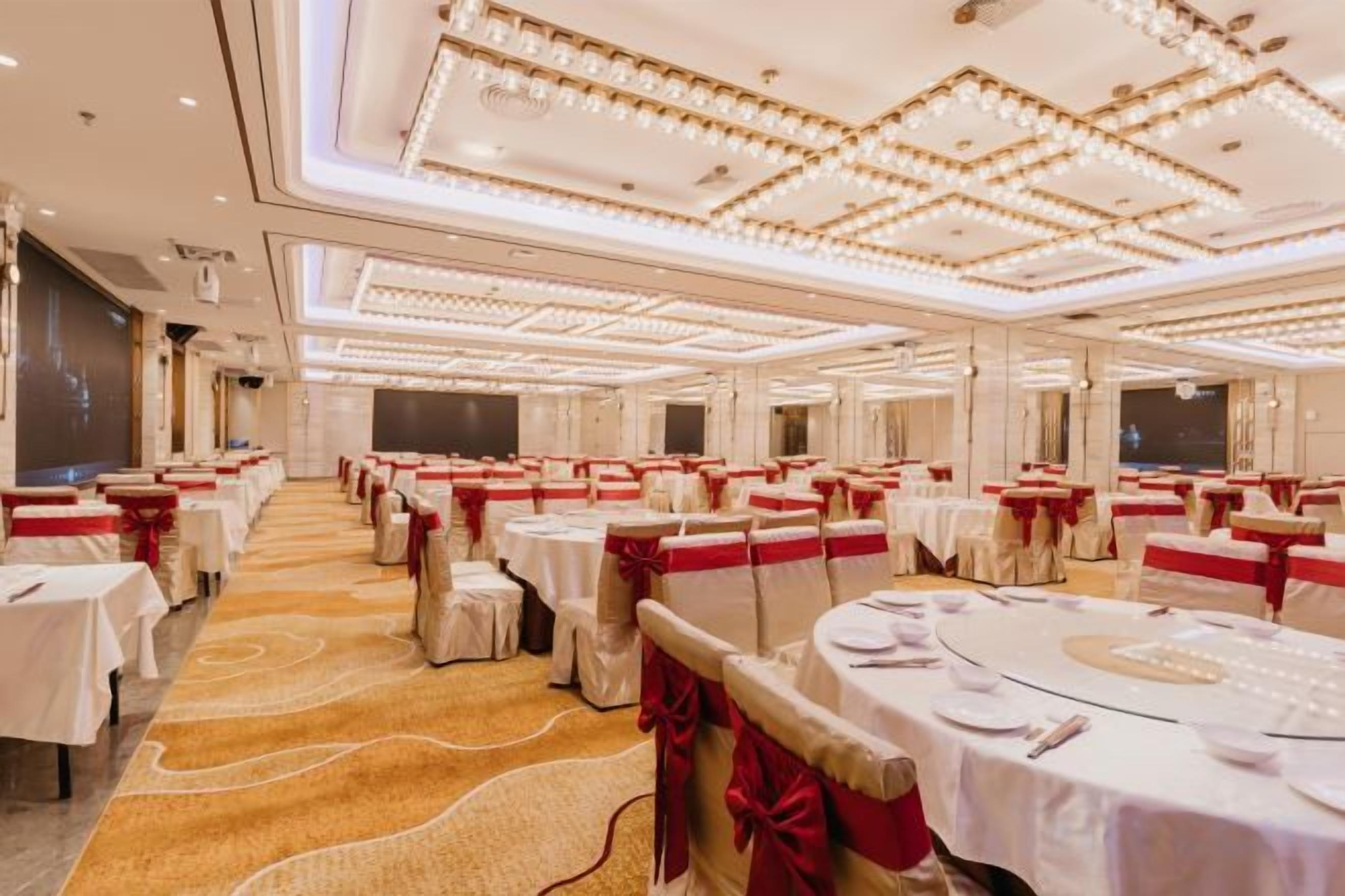 A banquet hall with round tables, red sashes, and a carpeted floor.