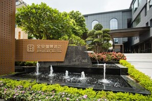 A hotel entrance with a sign, a water feature, and a landscaped garden. - Jinquan Yujing Hotel (Enping)
