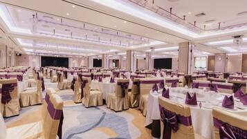 Un salón de banquetes con mesas redondas, sillas y un escenario.