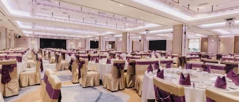 Un salón de banquetes con mesas redondas, sillas y un escenario.
