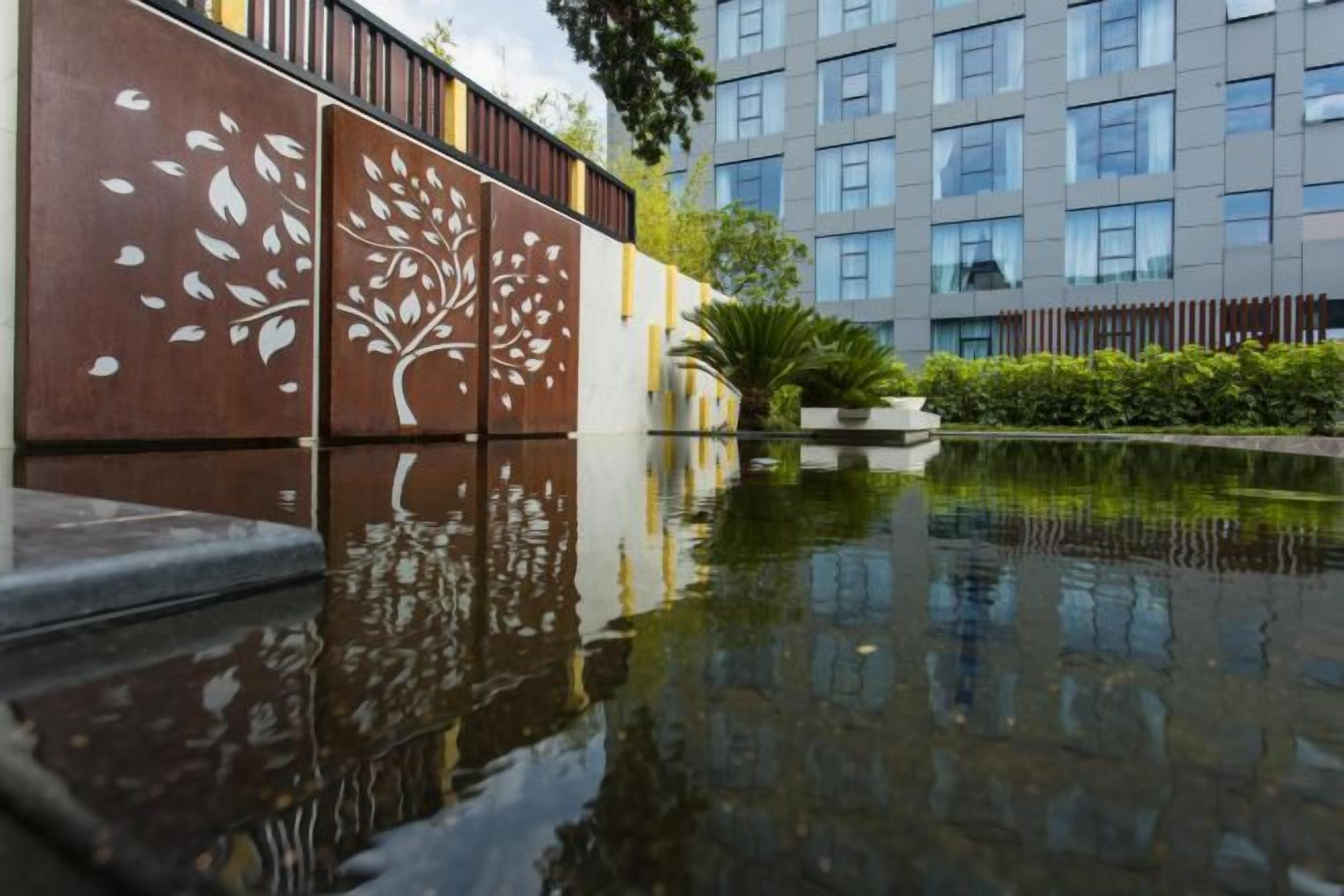 A reflective water feature with a tree design, a modern building in the background, and a well-maintained garden area.