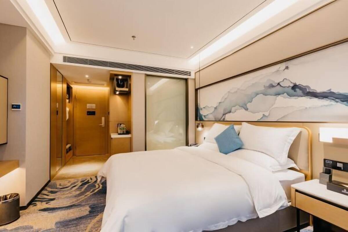 Ein Hotelzimmer mit einem großen Bett, einem Nachttisch, einem Wandfernseher und einem Gemälde über dem Bett.