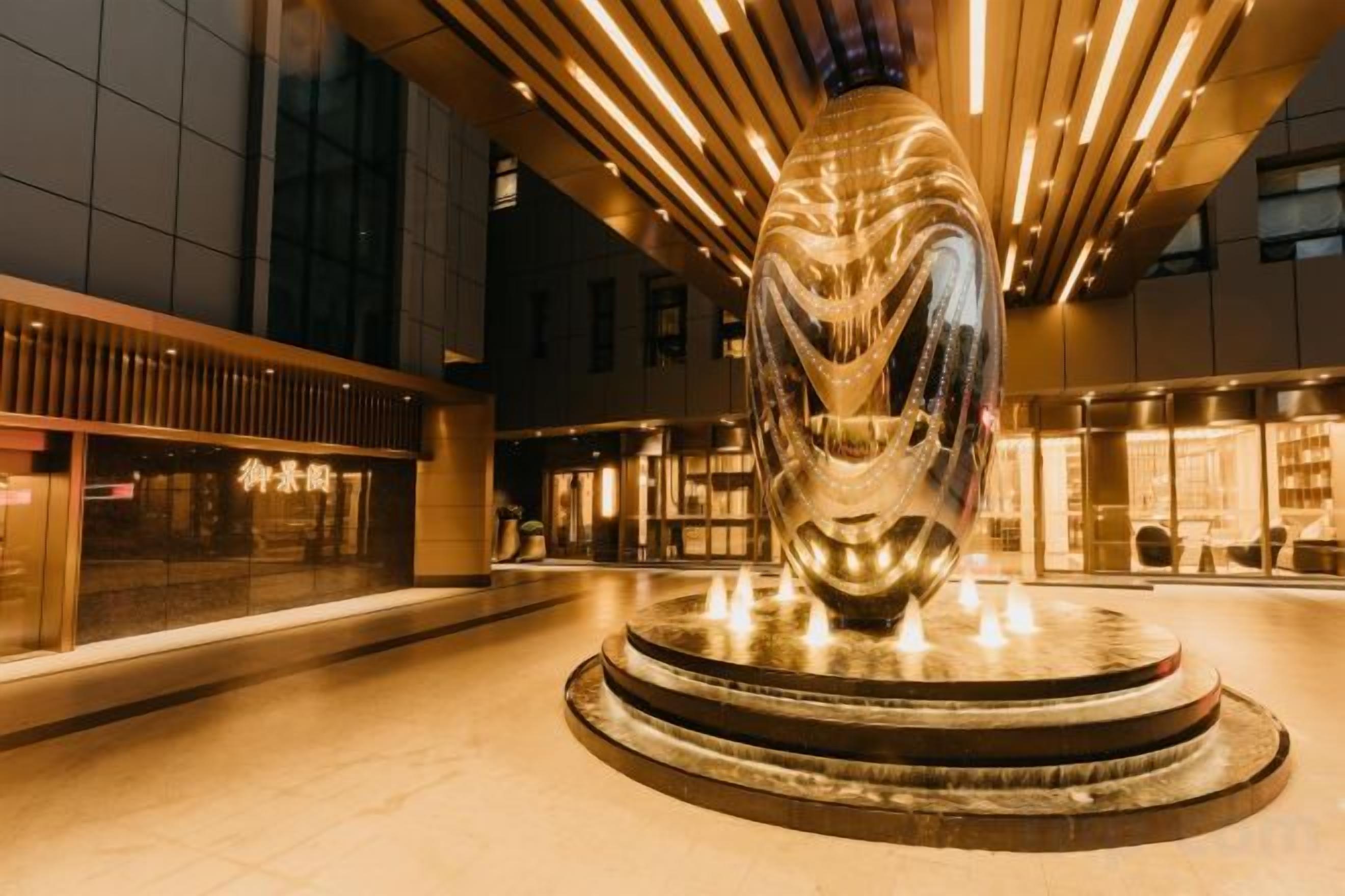 A modern building with a central sculpture, a fountain, and a well-lit interior.