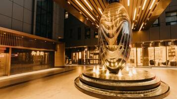 A modern building with a central sculpture, a fountain, and a well-lit interior.