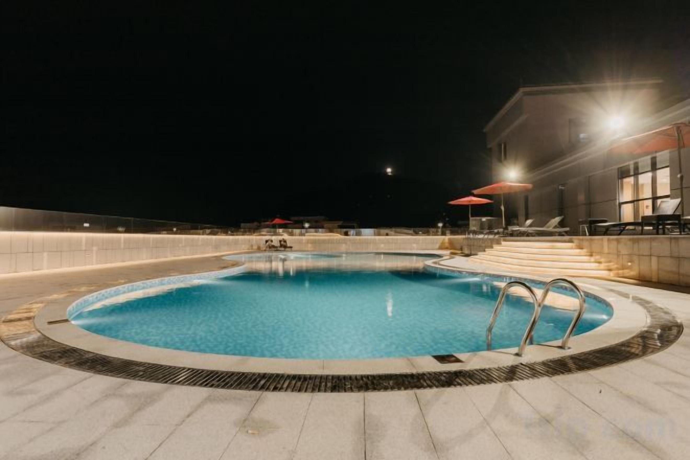 A swimming pool with steps leading into it, surrounded by a paved area with lounge chairs and umbrellas.
