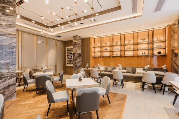 Un interior moderno con mesas y sillas dispuestas para comer, una pared de mármol y una estantería decorativa con objetos.