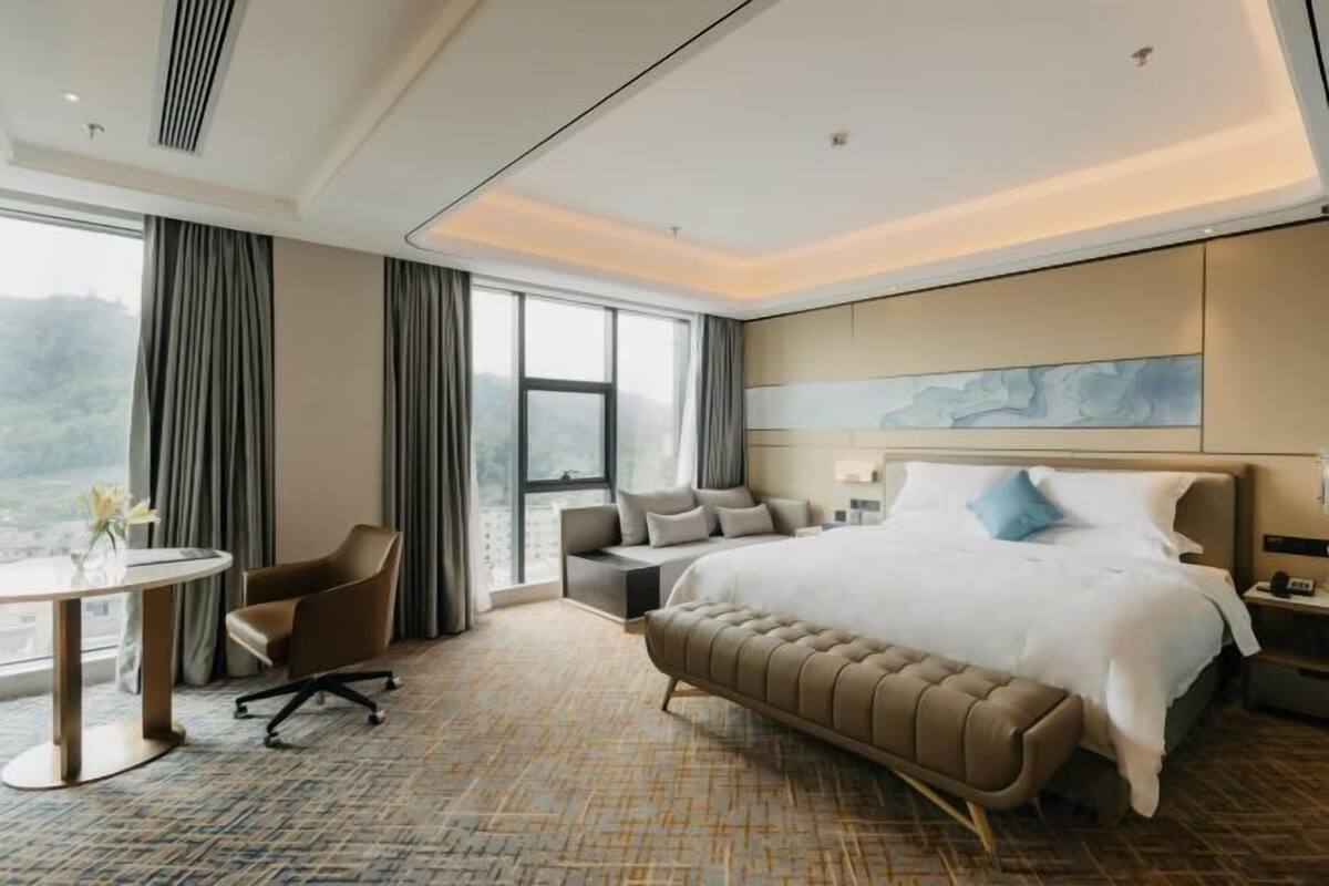 Ein Hotelzimmer mit einem großen Bett, einer Sitzecke, einem runden Tisch und Blick ins Freie.