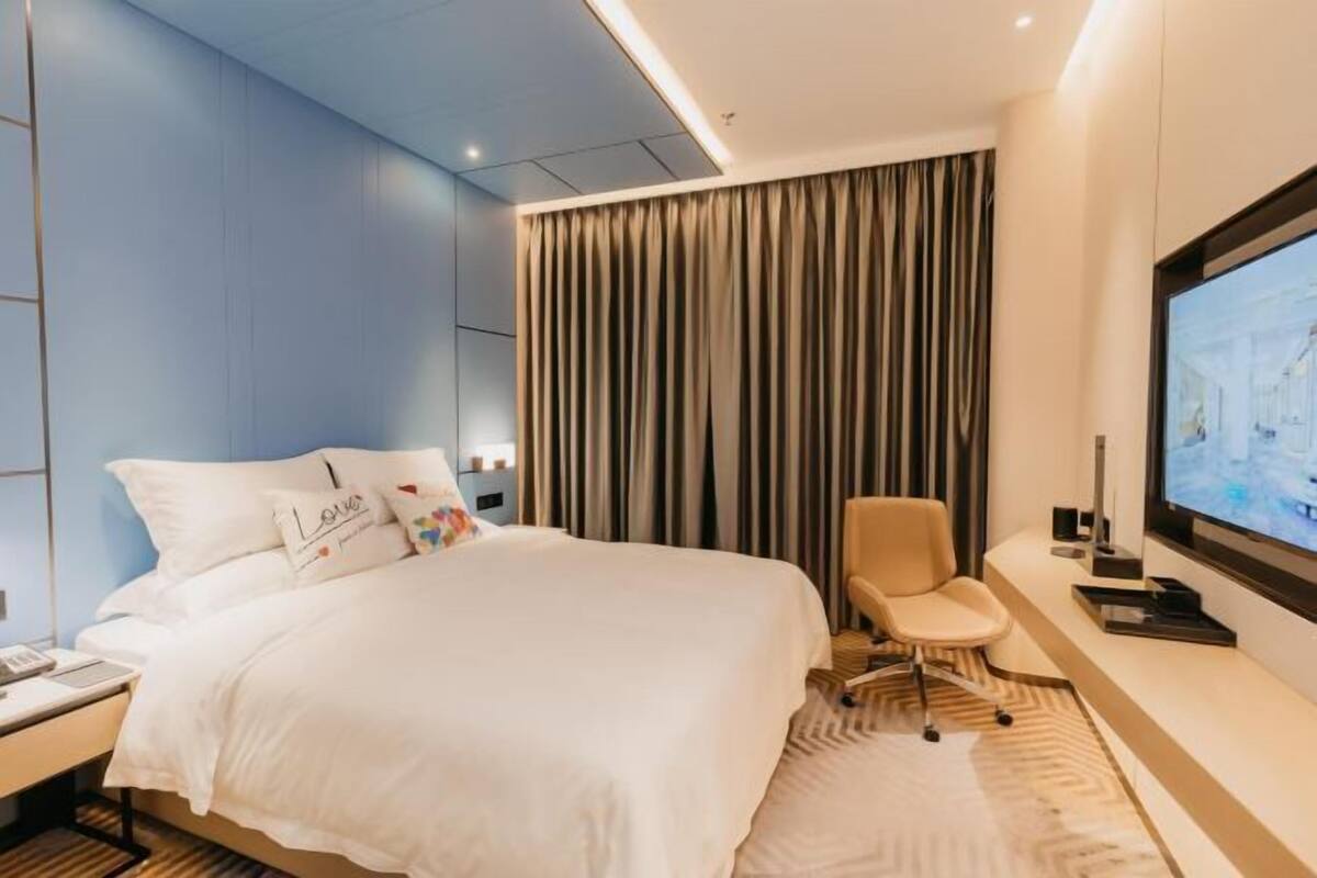 Ein modernes Hotelzimmer mit einem großen Bett, einem Schreibtisch, einem Sessel, einem Fernseher und einem Vorhang.