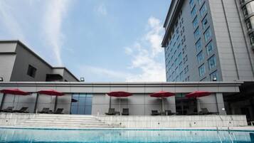 A swimming pool with lounge chairs and umbrellas, a building with a modern design, and a clear sky.