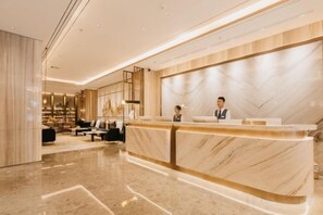 A hotel reception area with a marble reception desk, seating area, and a modern interior design. - Jinquan Yujing Hotel (Enping)