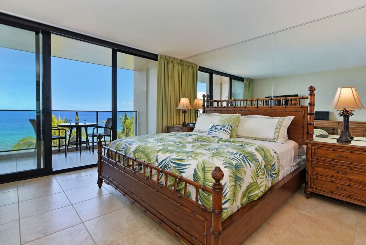 Una camera da letto con un letto grande, un comodino in legno, una sedia e vista sull'oceano.