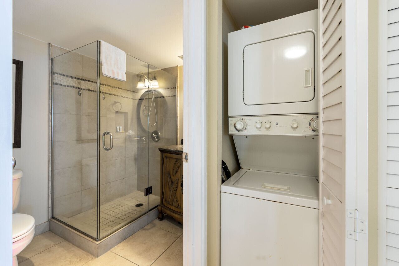 Un baño compacto con ducha de mampara de vidrio, inodoro y lavadora y secadora integradas.