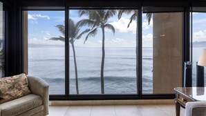A room with a large window offering a view of the ocean and palm trees. - Ocean Front - Gorgeous Views! (Lahaina)