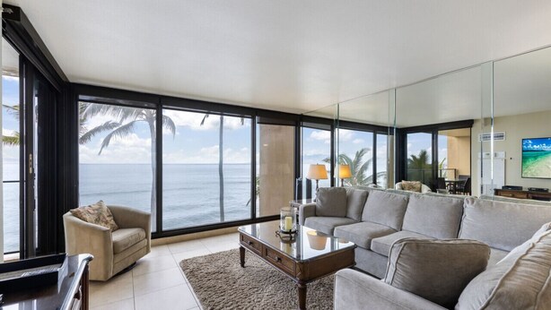A spacious living room with a large window overlooking the ocean, a comfortable sofa, a coffee table, and a television. - Ocean Front - Gorgeous Views! (Lahaina)