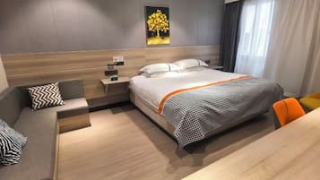A hotel room with a bed, a nightstand, a seating area with a sofa and chair, and a painting on the wall.