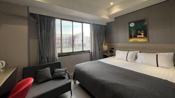 Ein Hotelzimmer mit einem großen Bett, einem Schreibtisch mit Stuhl, einem Fenster mit Vorhängen und einem Bild an der Wand.