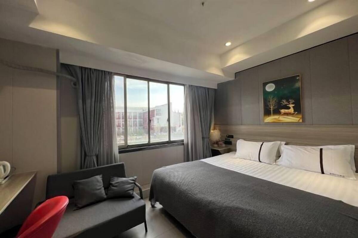 Une chambre d’hôtel avec un grand lit, un bureau avec une chaise, une fenêtre avec des rideaux et un tableau au mur.