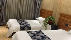 Ein Hotelzimmer mit zwei Betten, einem Holzkopfende, einer Topfpflanze und einem Vorhang.