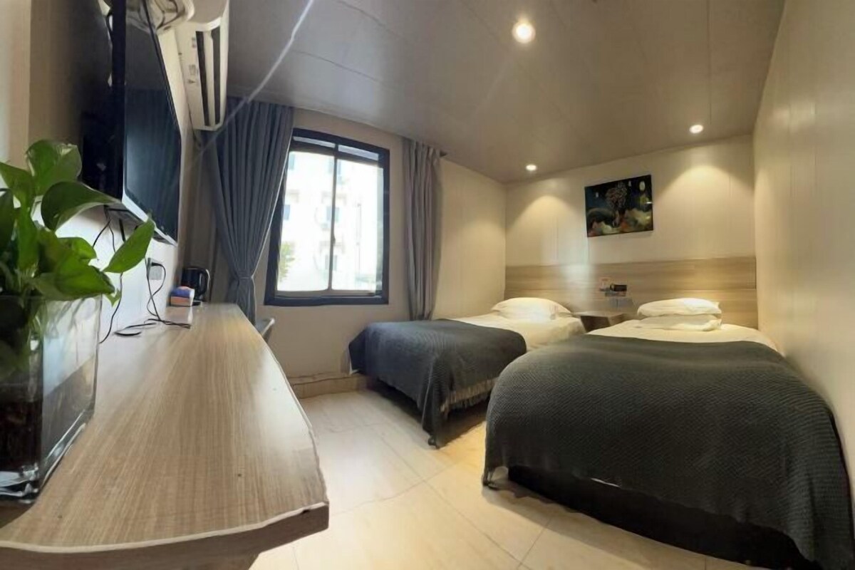 Habitación de hotel con dos camas, un escritorio, un televisor y una ventana con cortinas.
