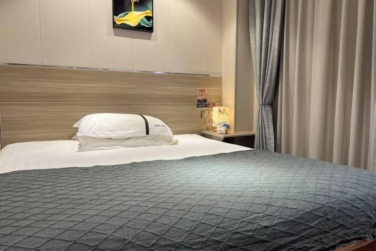 Une chambre d’hôtel avec un lit, une tête de lit, une table de chevet, une lampe et une fenêtre avec des rideaux.