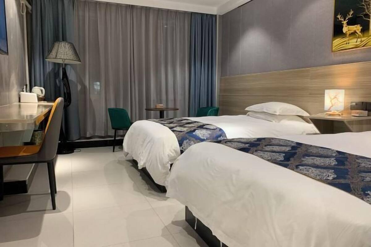 Une chambre d’hôtel avec deux lits, un bureau, une chaise, une lampe et une petite table.