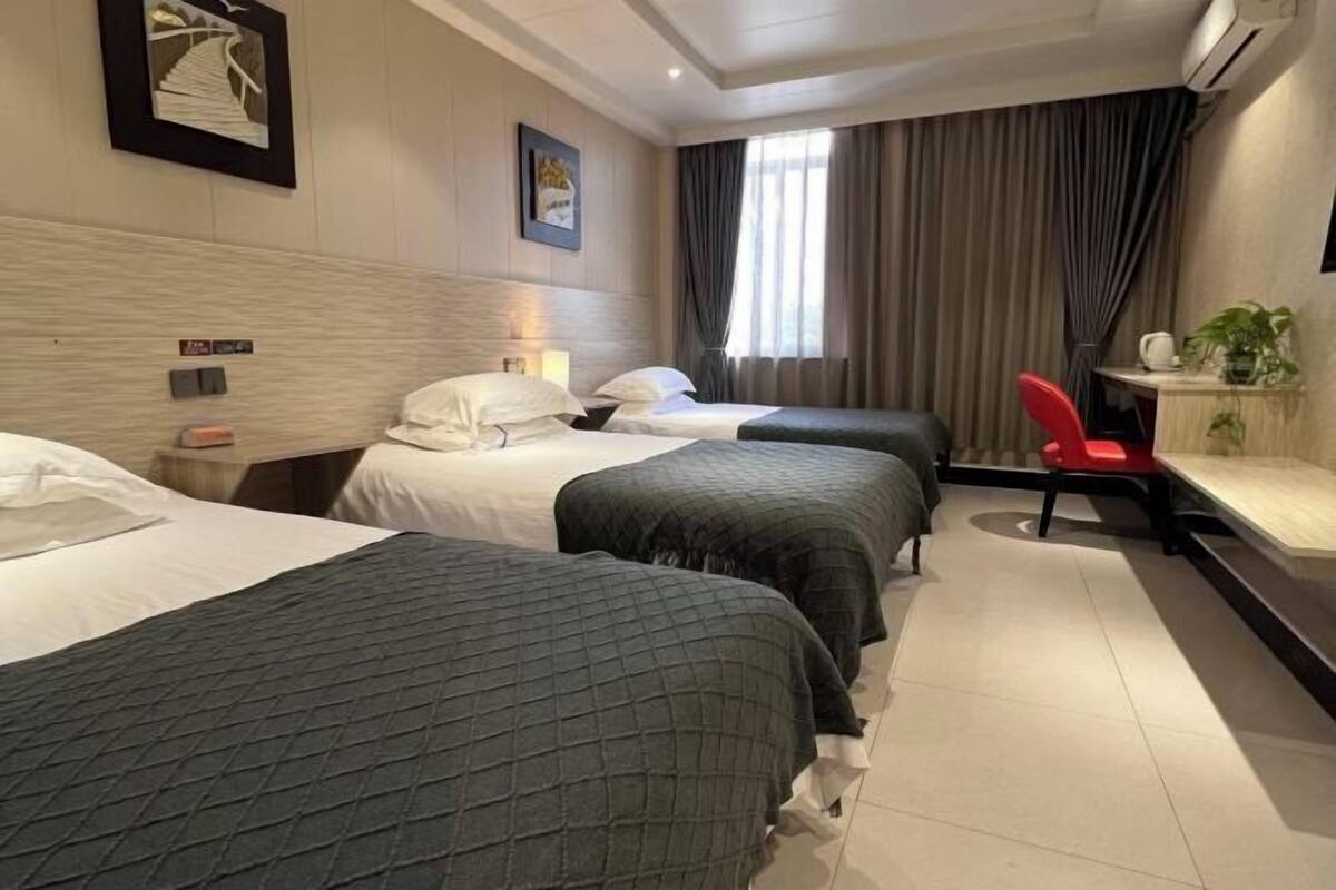 Une chambre d’hôtel avec deux lits, un bureau, une chaise, une fenêtre avec des rideaux et un climatiseur fixé au mur.