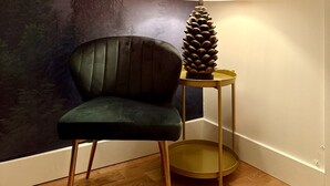 Una stanza con un murale a tema foresta, una poltrona verde scuro, una lampada con base a pigna e un quadro incorniciato con un cervo.