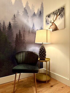 A room with a forest-themed wall mural, a dark green armchair, a lamp with a pinecone base, and a framed picture of a deer. - 1277 3rd Avenue · Spacious apartment with parking in Limoilou (Québec)