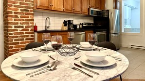 A modern kitchen with wooden cabinets, a brick accent wall, and a dining area set for four with wine glasses and plates.