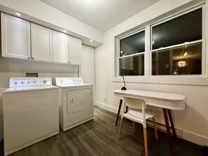 Una sala amb bugaderia, que inclou una rentadora, una assecadora i una taula petita amb una cadira.