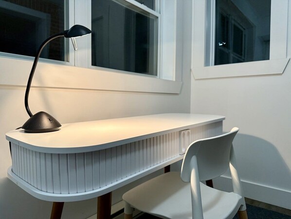 A modern, curved desk with a lamp, a white chair, and a window in a room with white walls.