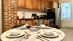 Una cucina moderna con mobili in legno, una parete decorata con mattoni e un'area pranzo per quattro persone, apparecchiata con bicchieri da vino e piatti.