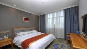 Una camera d'albergo con un letto, una scrivania, una sedia, un comodino e una finestra con tende.