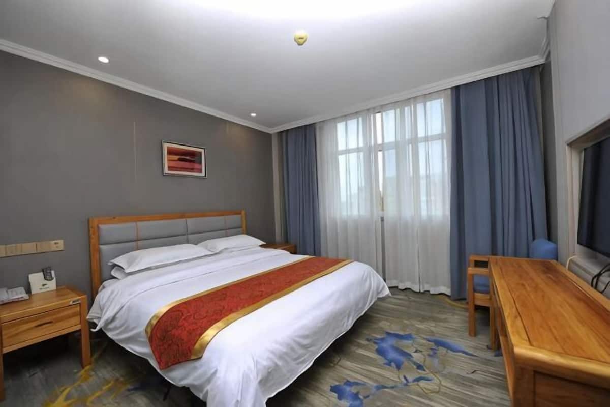 A hotel room with a bed, a desk, a chair, a nightstand, and a window with curtains.