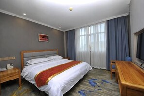 Habitación de hotel con cama, escritorio, silla, mesita de noche y ventana con cortinas.