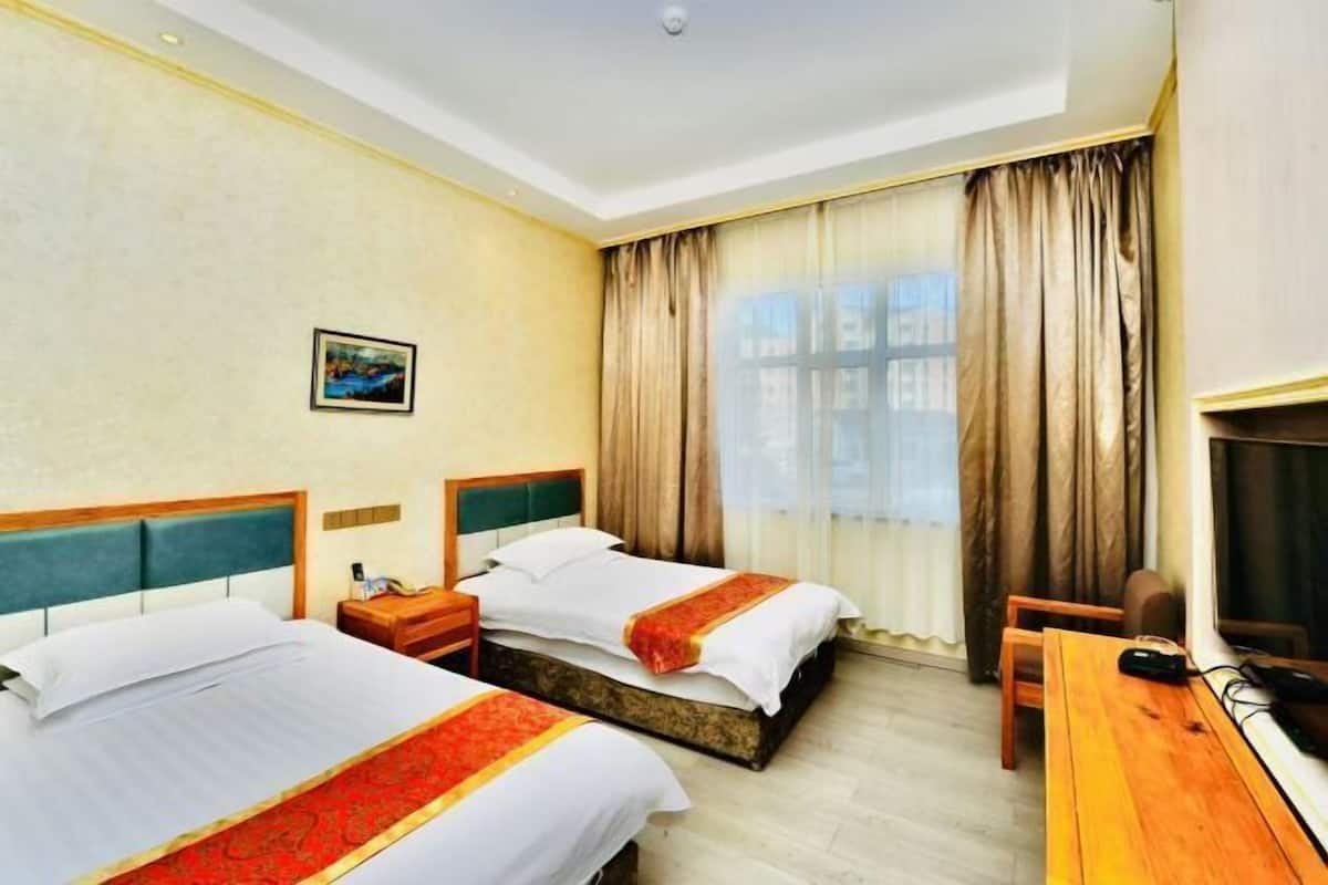 A hotel room with two beds, a desk, a chair, a TV, and a window with curtains.