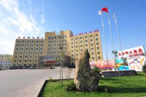 A multi-story hotel with a flat facade, a large rock feature in the foreground, and flags on poles. - You Yi Feng Hotel (Habahe)