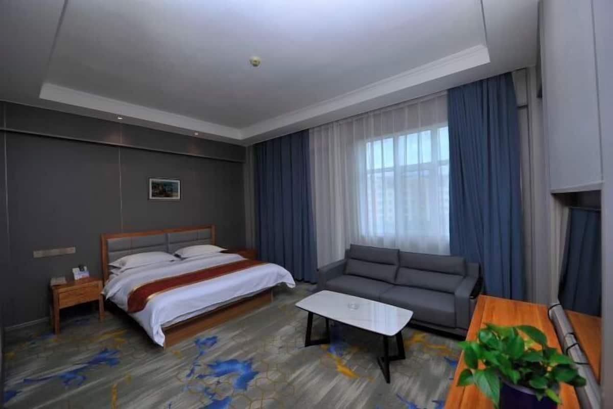 A hotel room with a bed, a sofa, a coffee table, a nightstand, and a potted plant.