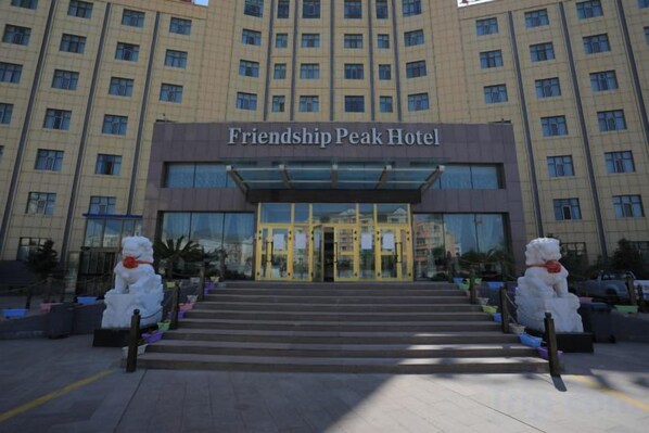 The Friendship Peak Hotel entrance with a glass facade and a set of stairs leading up to the doors.