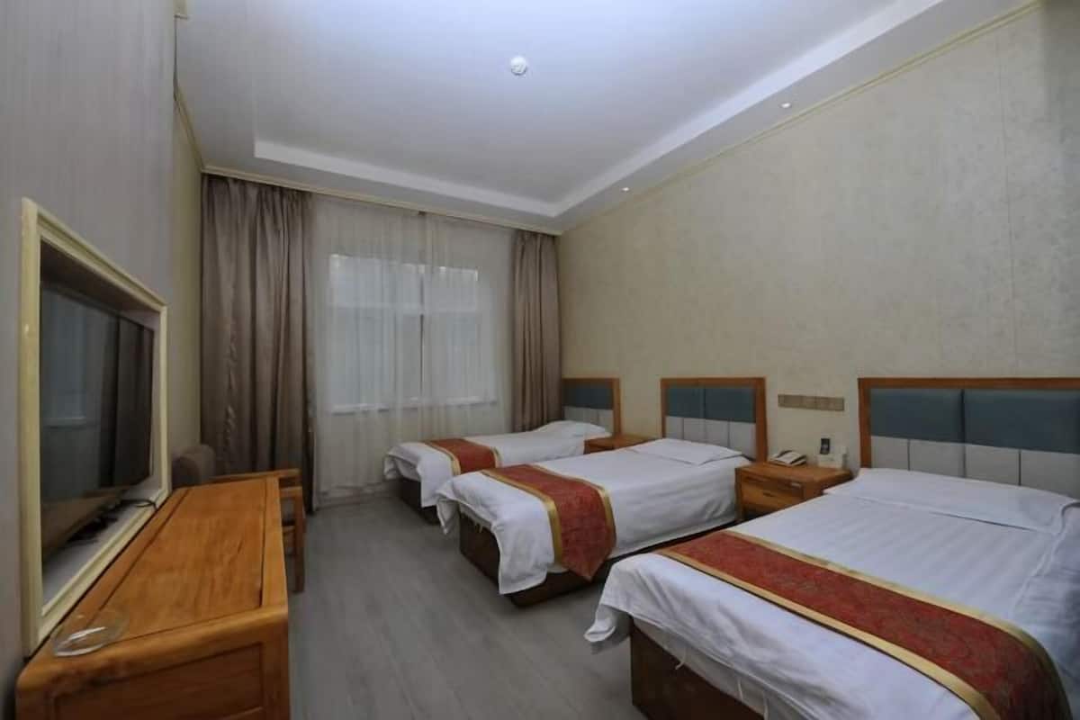 A hotel room with three beds, a TV, a desk, and a window with curtains.