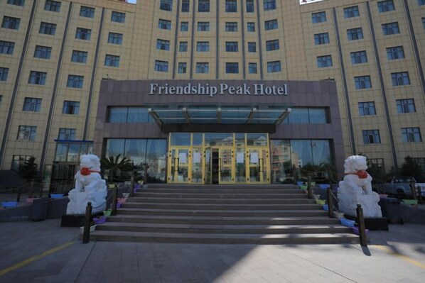 The Friendship Peak Hotel entrance with a modern glass facade and a symmetrical staircase leading up to the doors. - You Yi Feng Hotel (Habahe)