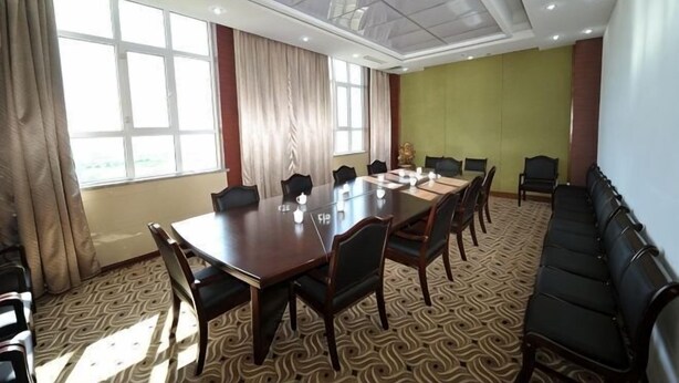 Egy nagy tárgylóasztallal, székekkel, egy kanapéval és mintás szőnyeggel berendezett konferenciaterem.