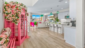 A modern kitchen with white cabinets, a central island with bar stools, and a pink decorative structure with floral arrangements. - Specials Barbie themed, Lakefront, games+pool (Indio)