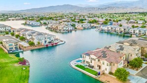 A residential area with houses along a river, featuring a mix of single and multi-story buildings, some with visible balconies and solar panels. - Specials Barbie themed, Lakefront, games+pool (Indio)