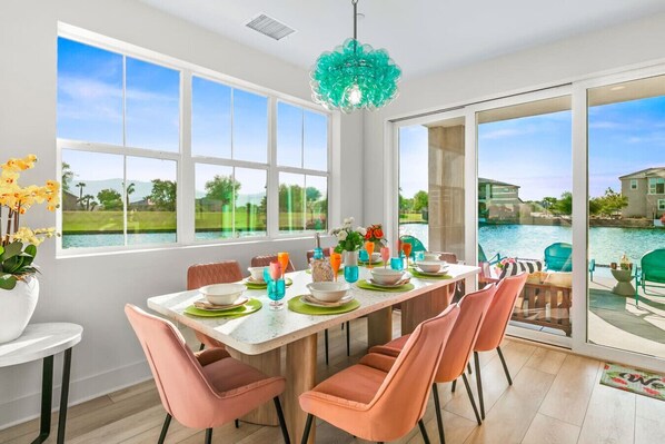 A dining area with a view of a swimming pool and a house.
