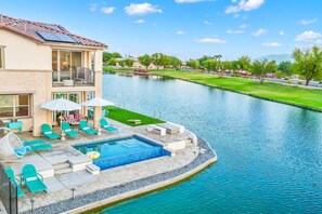 A two-story house with a swimming pool, outdoor furniture, and a view of a river.