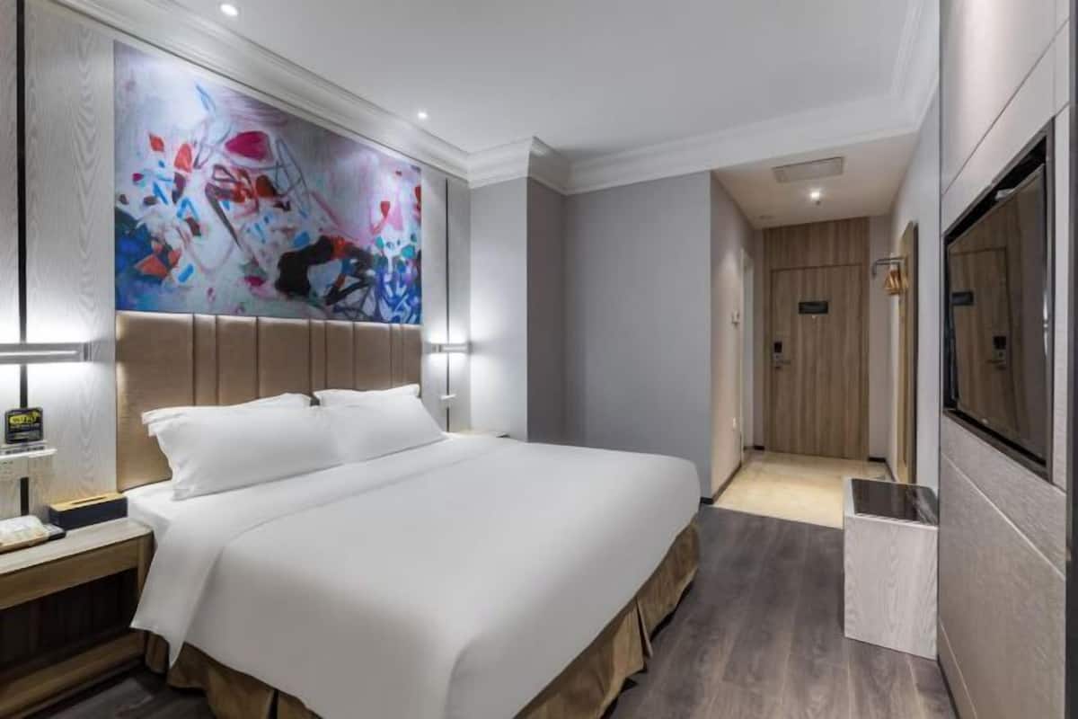 Hotellihuone, jossa on suuri sänky, yöpöytä, seinälle asennettu televisio ja ovi, joka johtaa käytävään.