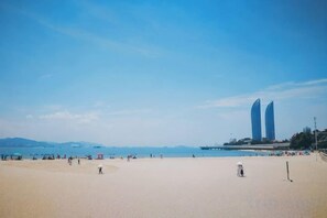 Uma praia com céu claro, areal arenoso e dois edifícios destacados ao longe.