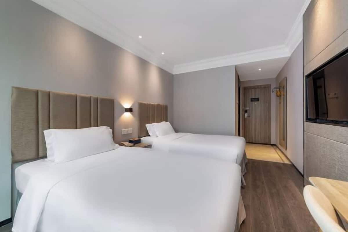 Hotellihuone, jossa on kaksi sänkyä, puulattia, televisio ja käytävä, joka johtaa kylpyhuoneeseen.